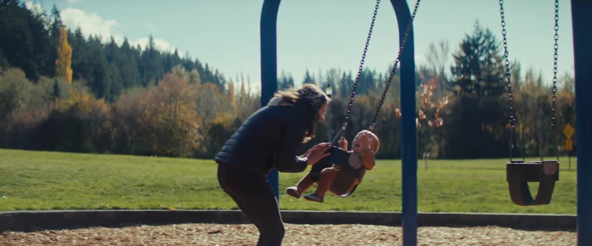 A mother pushes her son on a swing set at a park on a sunny autumn day