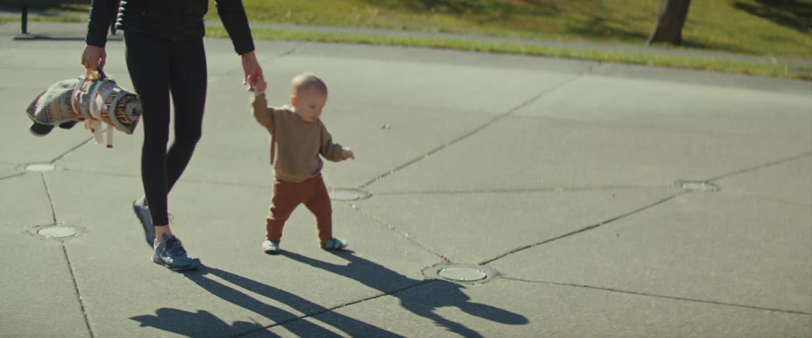 Male baby trying to talk by holding hands with a female adult then going to the floor and crawling on its own outdoors during day time