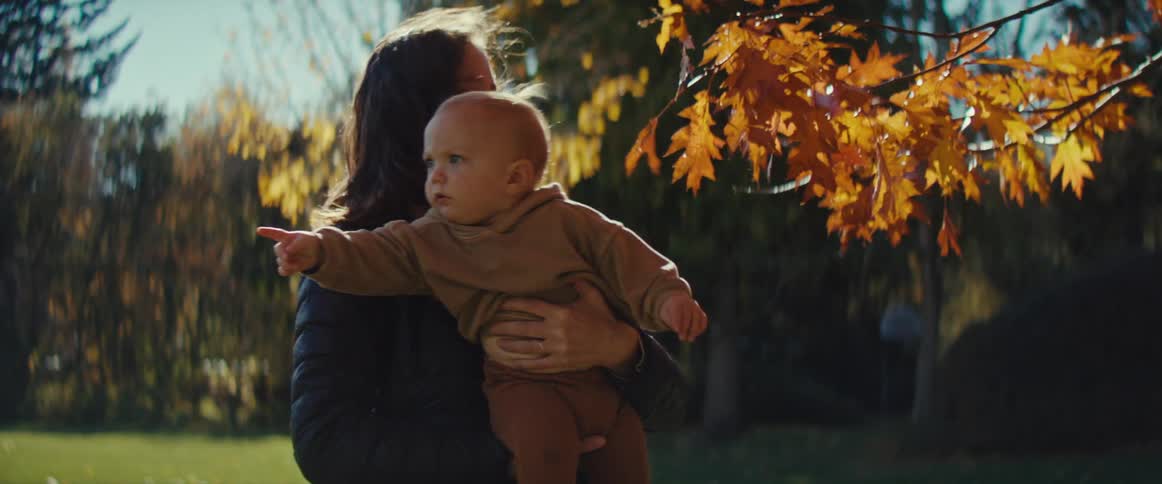 Mother carrying her child turns after the boy touches autumn leaves before pointing in a different direction
