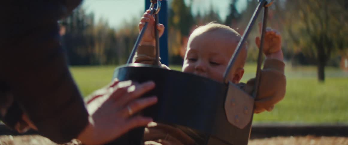 A happy baby is seen giggling and enjoying a swing in a park on a sunny day an adults hands gently push the swing keeping a watchful eye