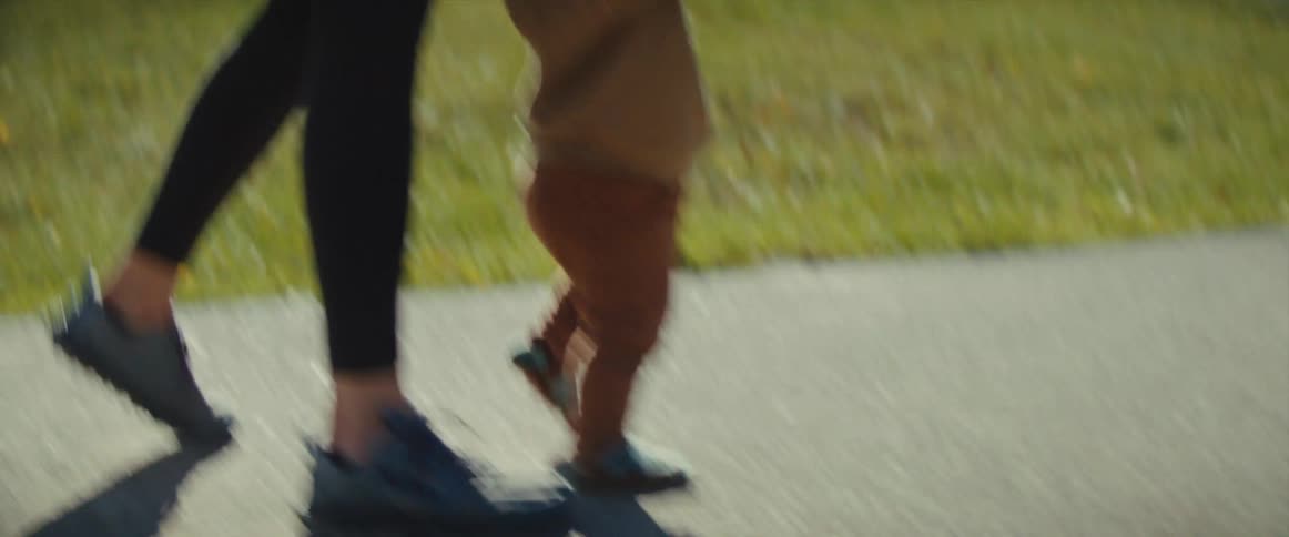 A mother holding her babys hand as the baby learns to walk in an outdoor park