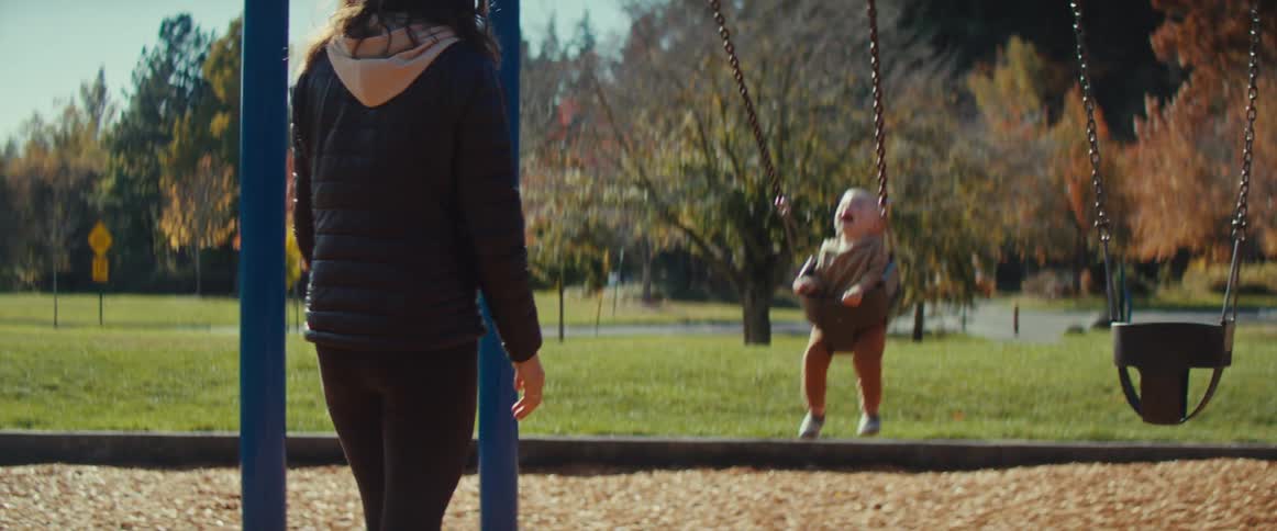 Mother swinging her baby on swingset at park on a fall day