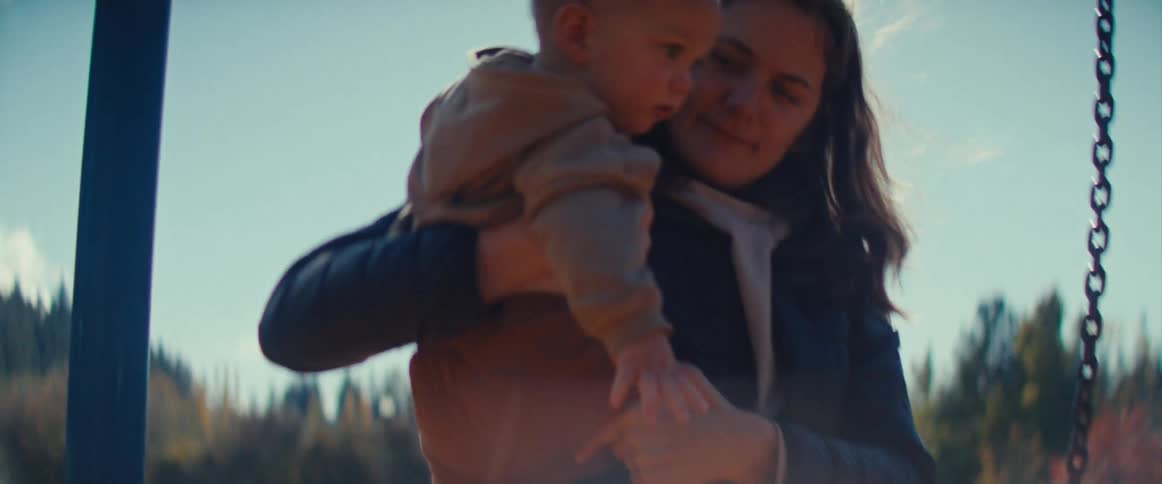 A woman takes her child out of a swing at a park