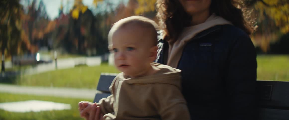 A mother carries her baby on her lap while sitting on a bench in a public park at midday