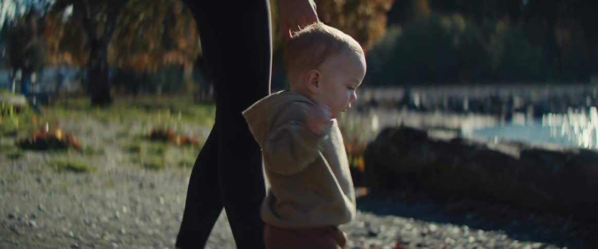 Child takes first steps beside an adult in a sunny park