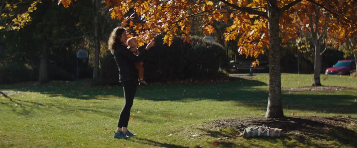 Woman holds a child while reaching for the leaves of an autumn tree