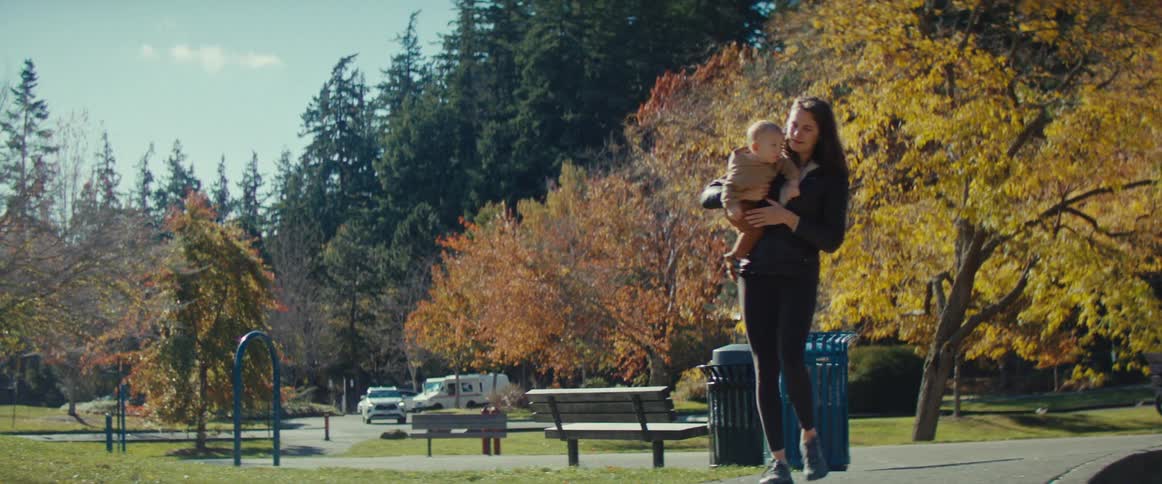 A woman picks up her child and walks to the playground in a park