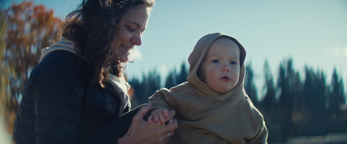 A mother and her child outdoors both happy the baby holding a stone in their hand and pointing toward the sky