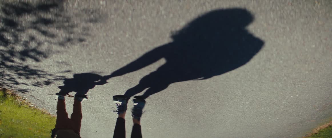 A mothers shadow is visible as she walks with her baby on a paved road on a sunny day