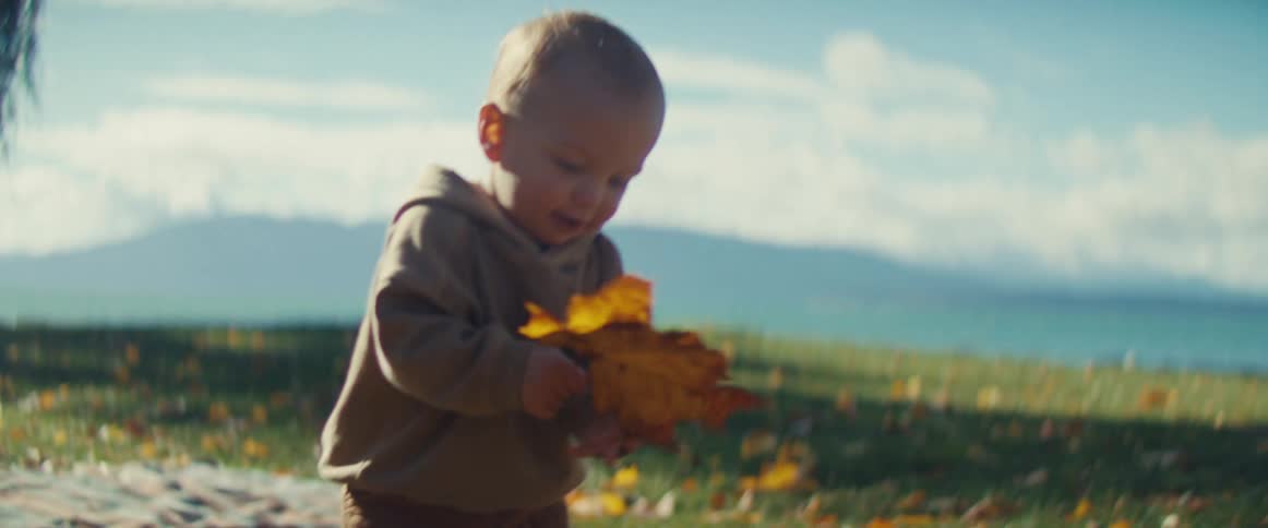Mother and son play with fallen leaves while fog obscures the mountains in the distance