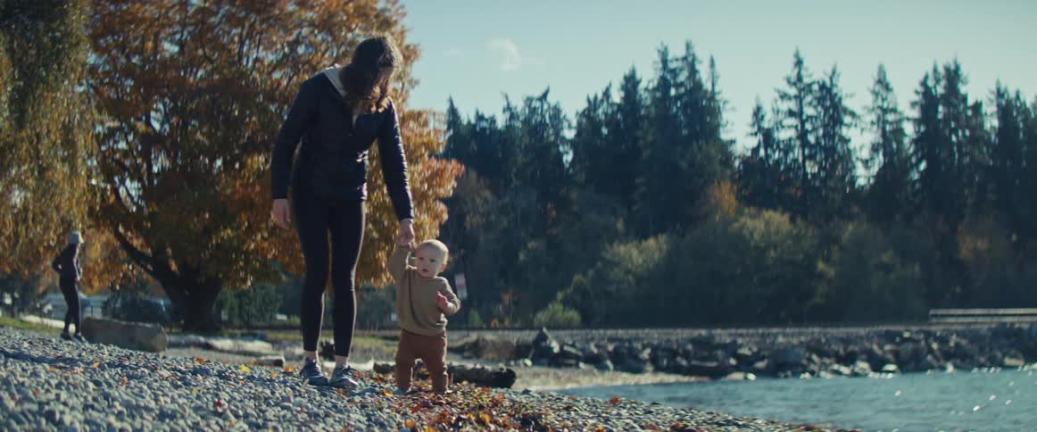 Mother and toddler walking on rocky shoreline near lake in the wilderness