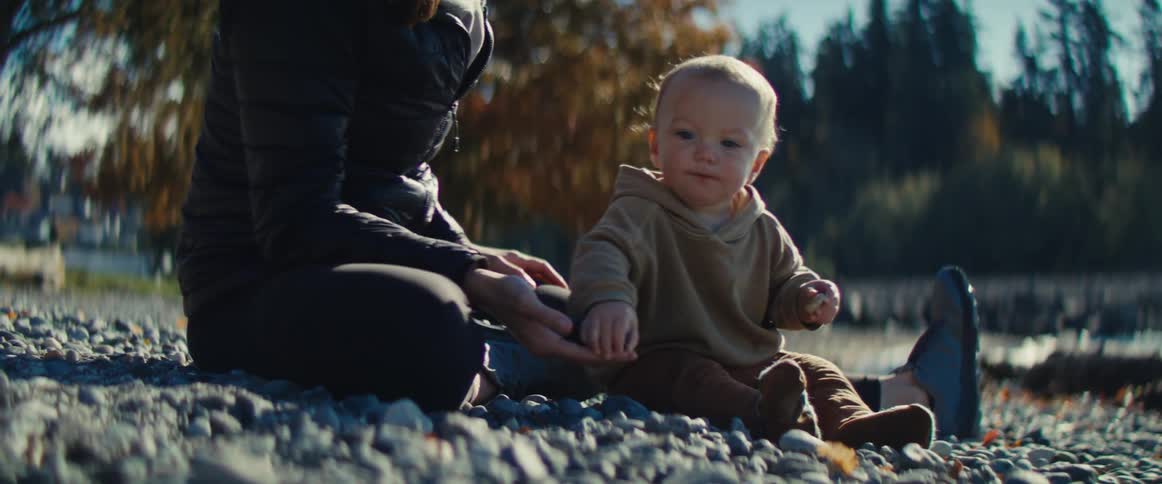 A mother sitting on the ground with her baby as the baby picks up a stone and puts it in their mouth
