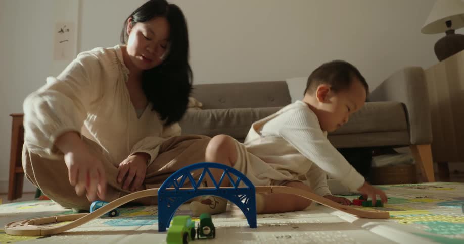 A mother and son play with a wooden train set on the floor in a cozy living room