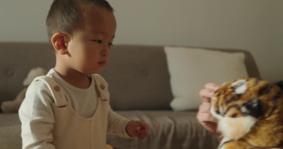A mother and her son playing with a stuffed tiger toy in the living room