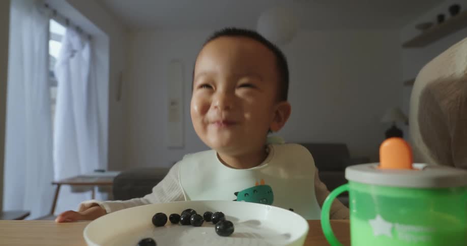 Happy toddler putting blueberries in his mouth and smiling
