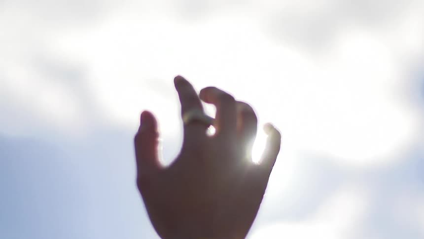 Persons hand raises towards a cloudy sky