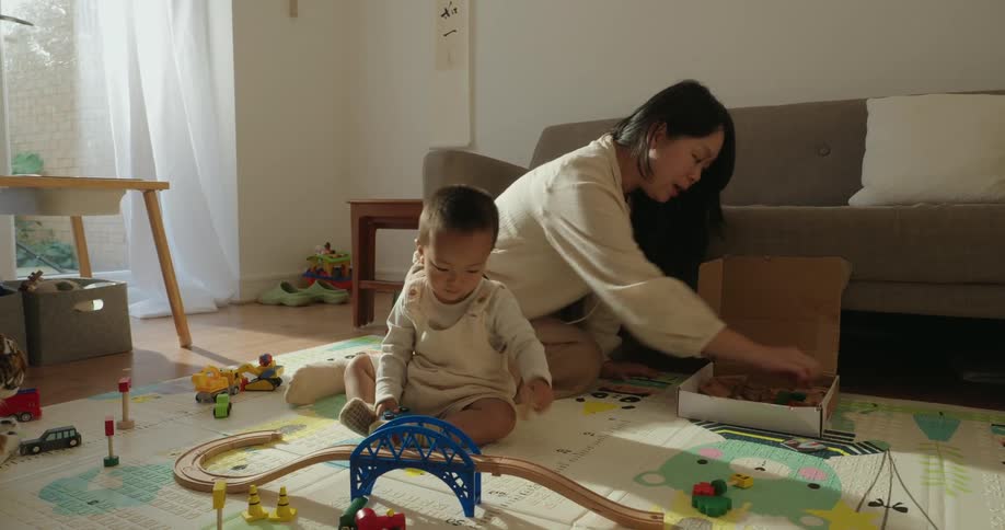 Mother helping her toddler play on the floor in warm home lighting