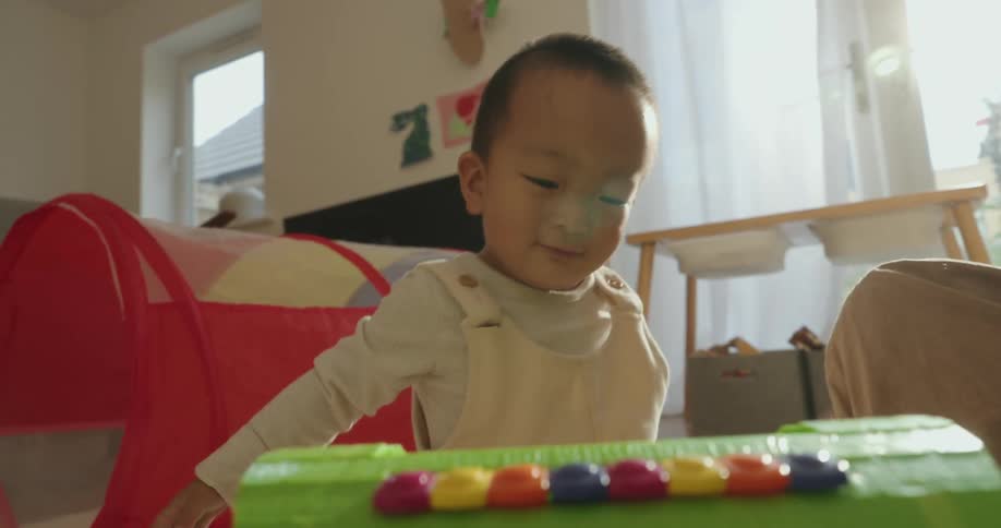 Toddler playing with a play set smiles as his mother plays along with him