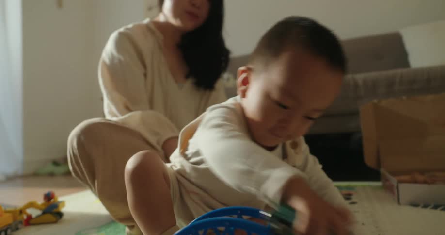 Child plays with a toy car while the mother watches sitting on the floor