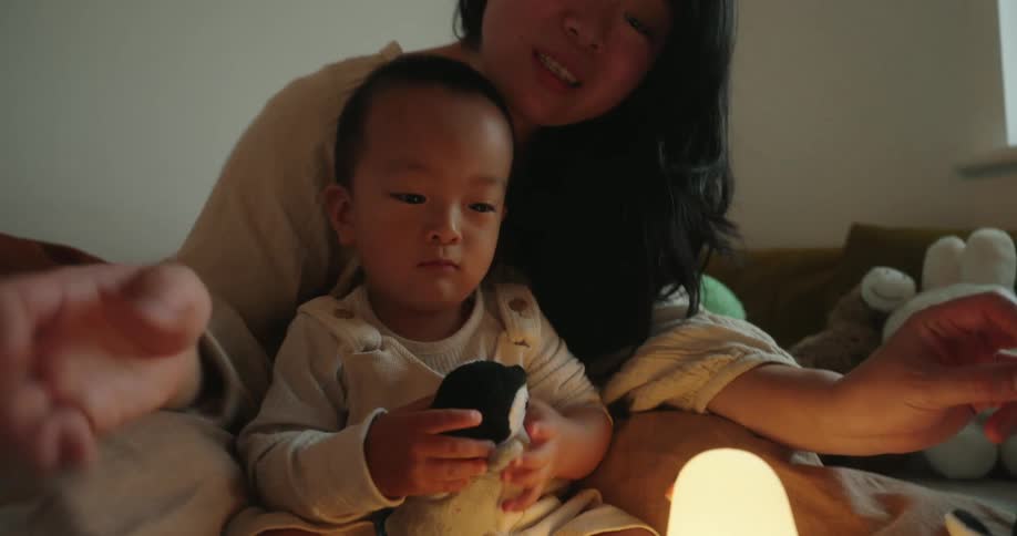 Mother and son sitting together on the bed with toys and soft lighting