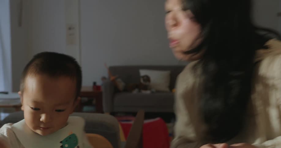 An asian baby eating at a table with his mother in a living room