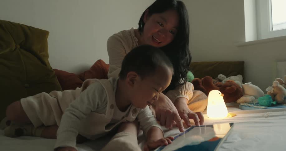 Mother and son lying on the bed reading a book lit by soft light