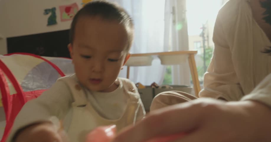 An asian mother and her son playing with a collection of toys while sitting on the bed in the bedroom at midday