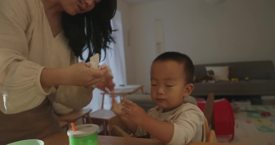 A woman takes a cup from a baby then starts wiping off his hands