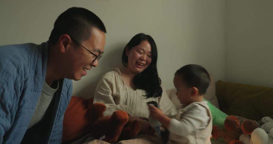 A family sitting together on the couch the young son holding a stuffed animal and asking his mom and dad to kiss it