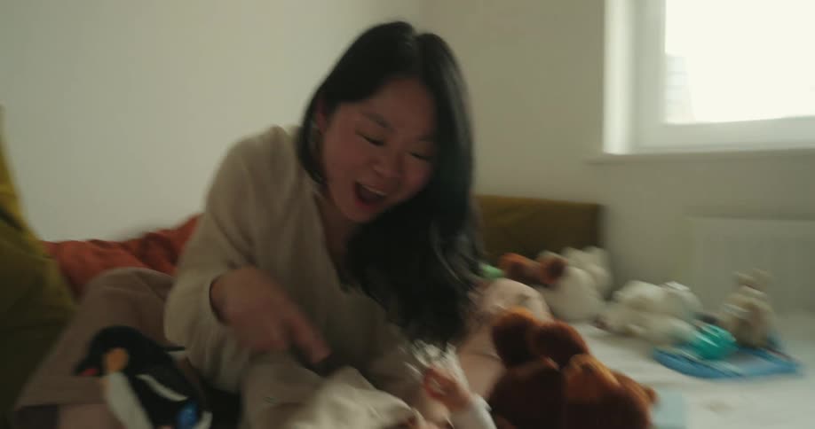 Woman playing with a child on the bed surrounded by toys
