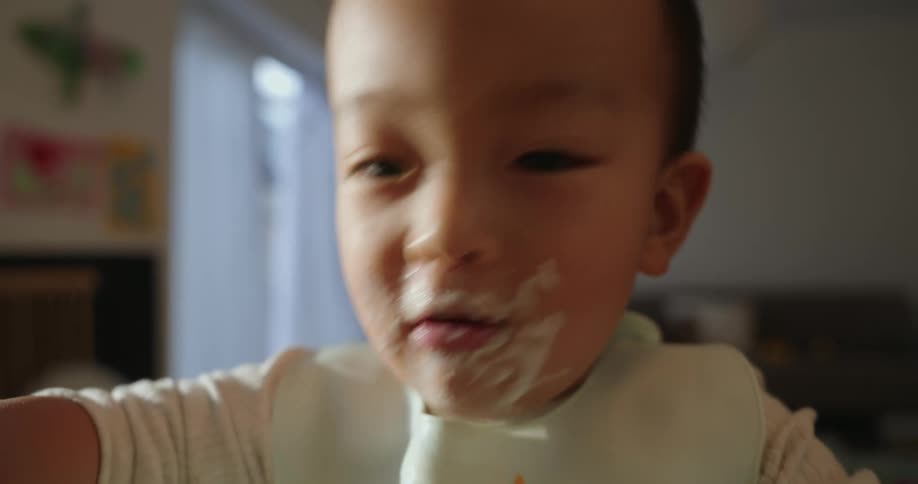 A baby happily eats with messy hands while sitting at a table in a cozy home