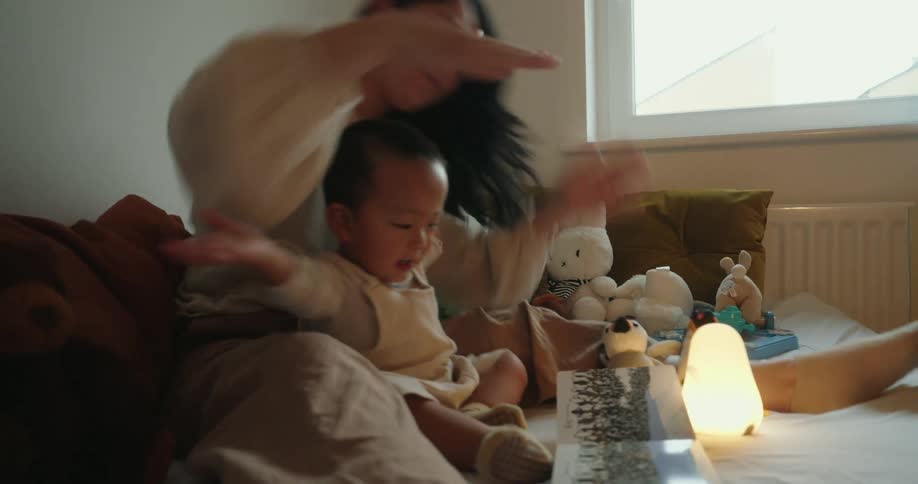 A happy mother and her toddler read a book together on the bed