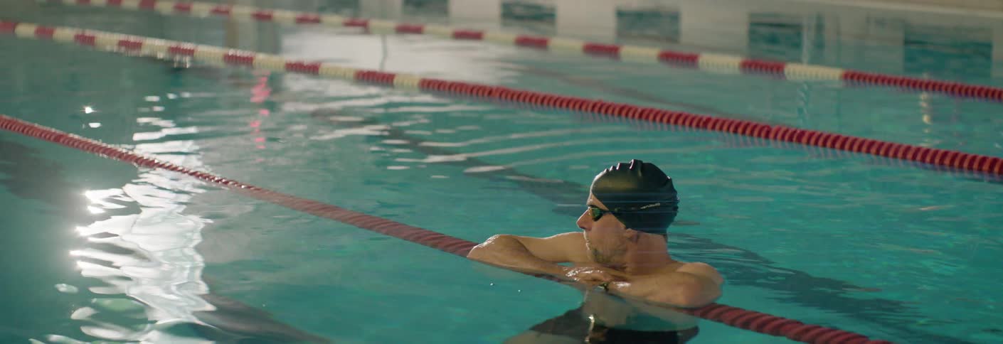 A man wearing a swim cap and swimming goggles in an olympic pool