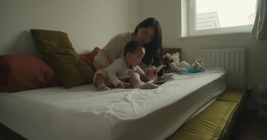 A mother and her baby play with stuffed toys on a bed in a cozy bedroom