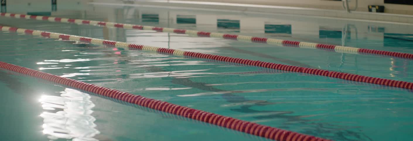 Indoor pool with red and white lanes reflecting light on the calm water