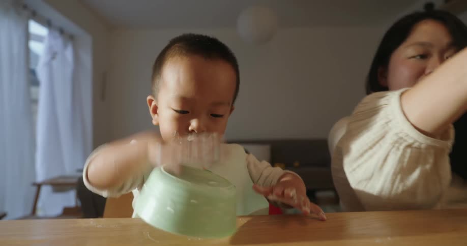 Mother cleans the face of her son after the child upends his food bowl while at home