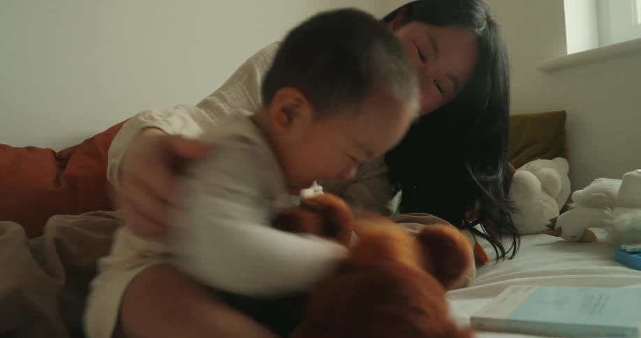 A mother playing with her son using a toy on the bed in the bedroom at midday