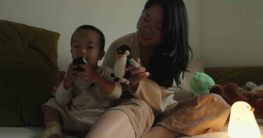 A mother and her child playing on a bed with stuffed animals
