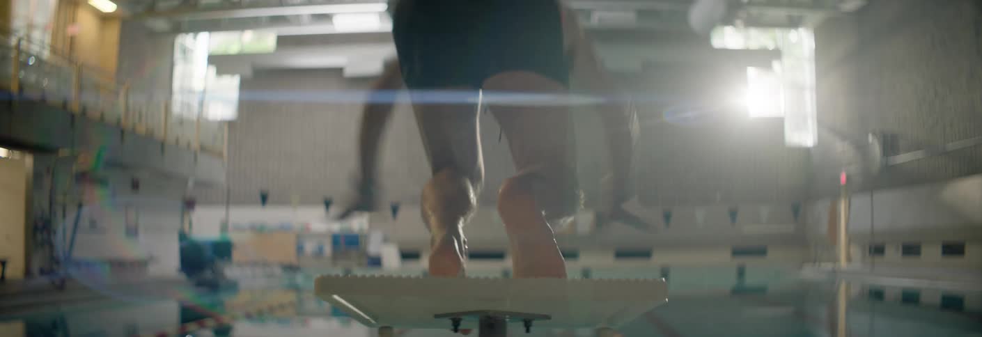 Athlete dives from a platform at an indoor pool