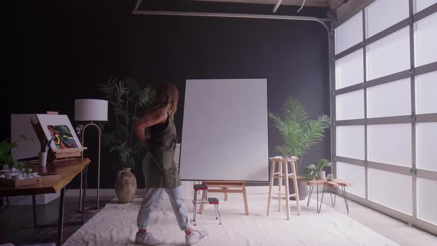 A young female artist preparing to start a large canvas painting in an art studio