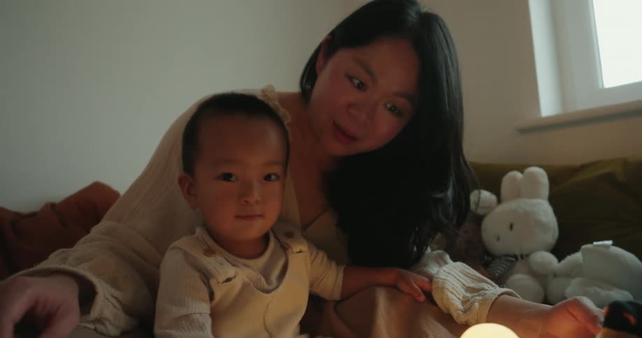 Mother plays with her young son holding plush toys on the bed