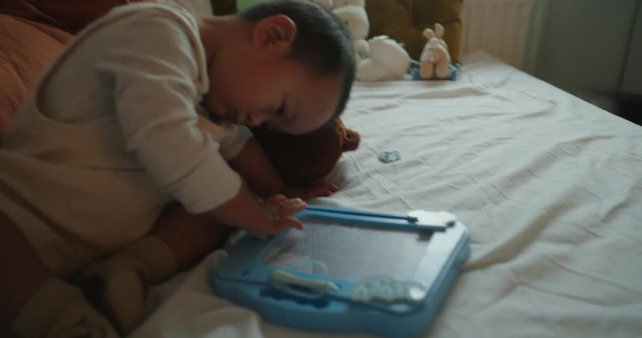 A little boy is in bed with some teddy bears and playing with a blue coloring object