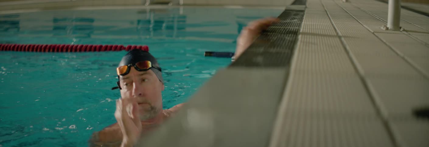 A man wearing a black swimming cap reaches the end of the lane and removes his goggles