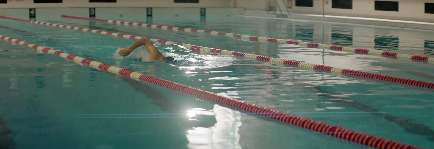 A lone swimmer glides down a quiet indoor lap pool between red and white lane lines