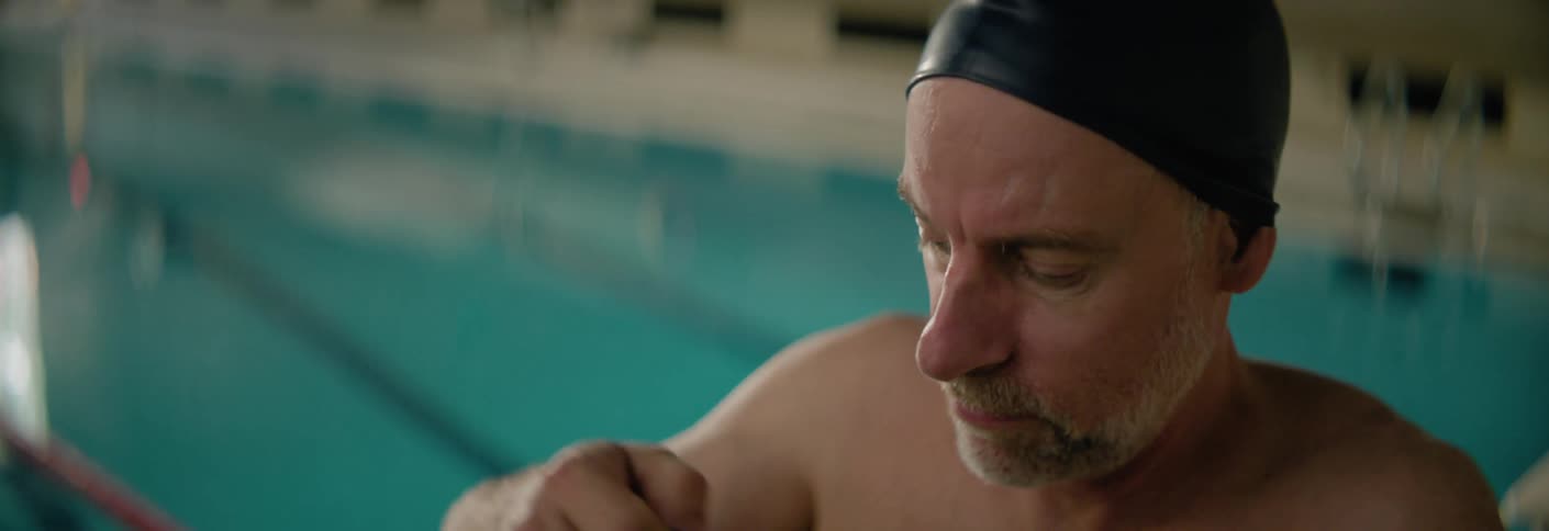 Man adjusts his swimming cap and goggles beside the pool before swimming