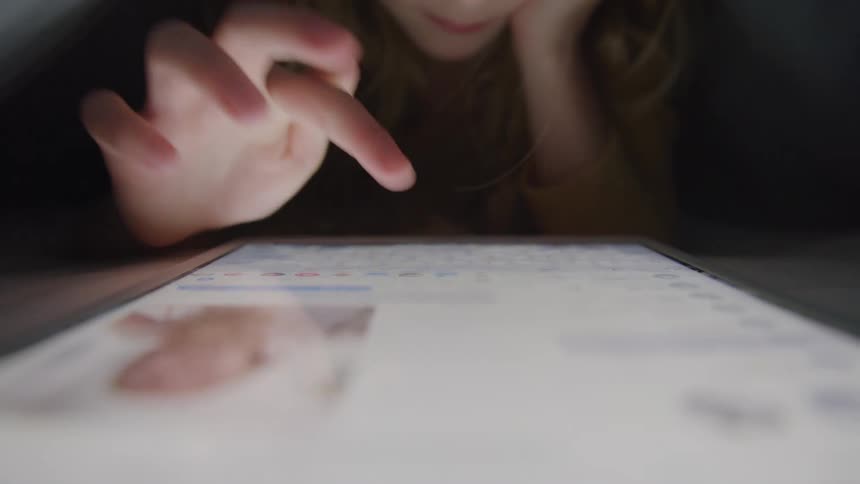 A girl lying down and using a tablet that is on the floor