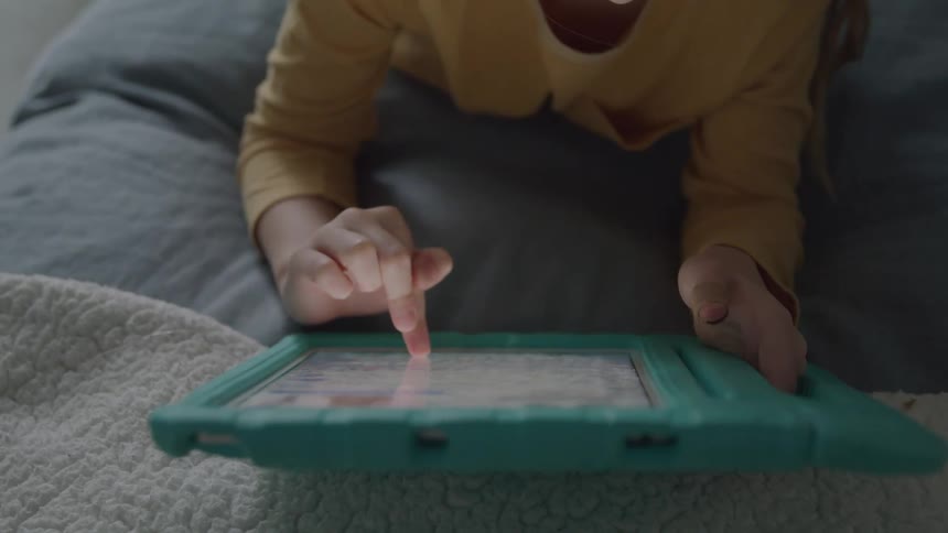 A child lying on the bed using a tablet in the bedroom at midday