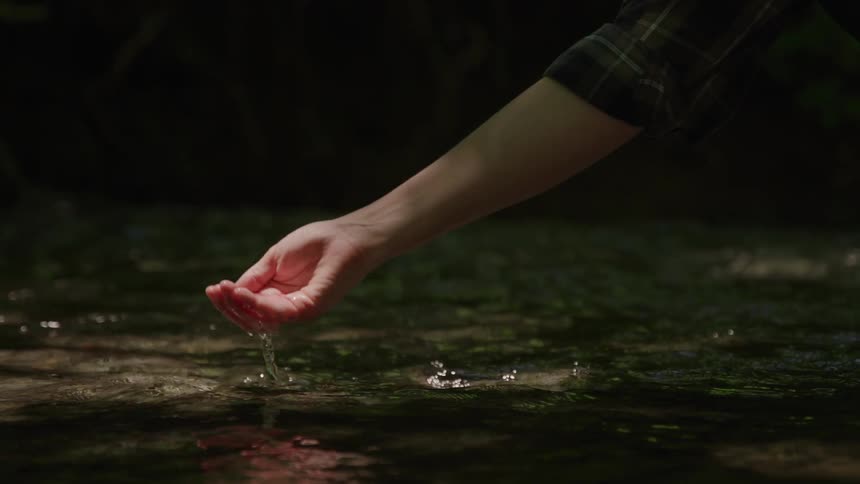A person reaches into a shallow stream to scoop up some water