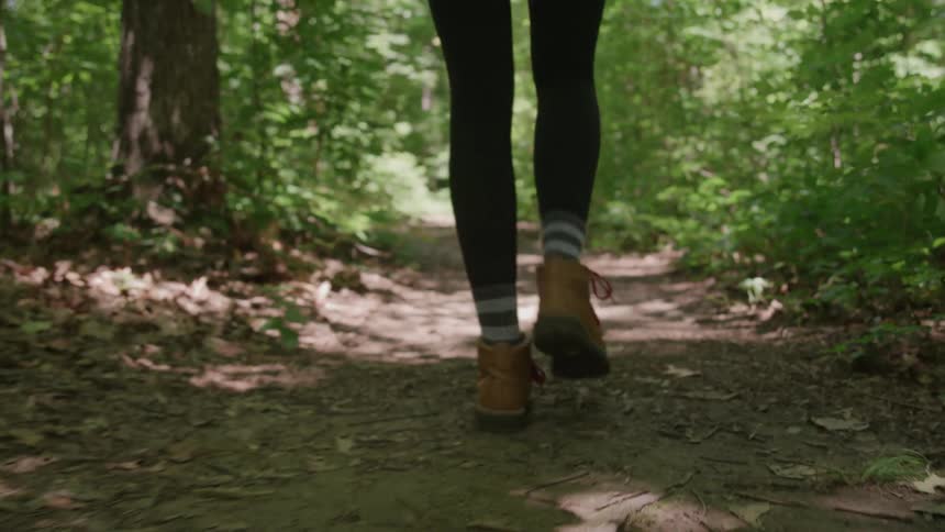 Feet and legs of a young woman walking on a trail through the woods