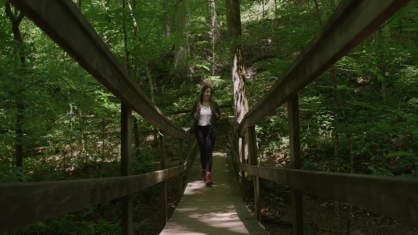 Woman walking across a wooden bridge in a lush green forest